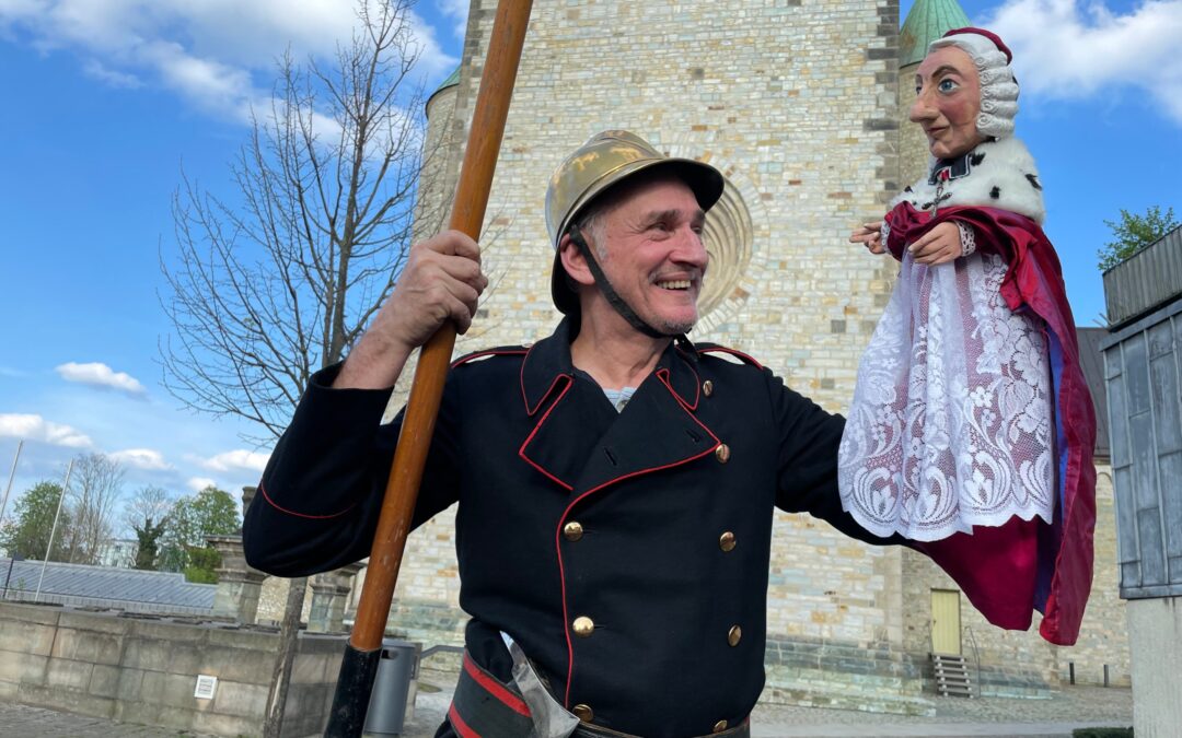 Puppenspieler als historischer Feuerwehrmann mit Fürstbischof-Handpuppe vor dem Paderborner Dom